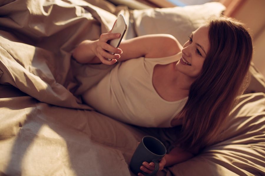 Mujer en la cama mirando en su móvil aplicaciones para ligar